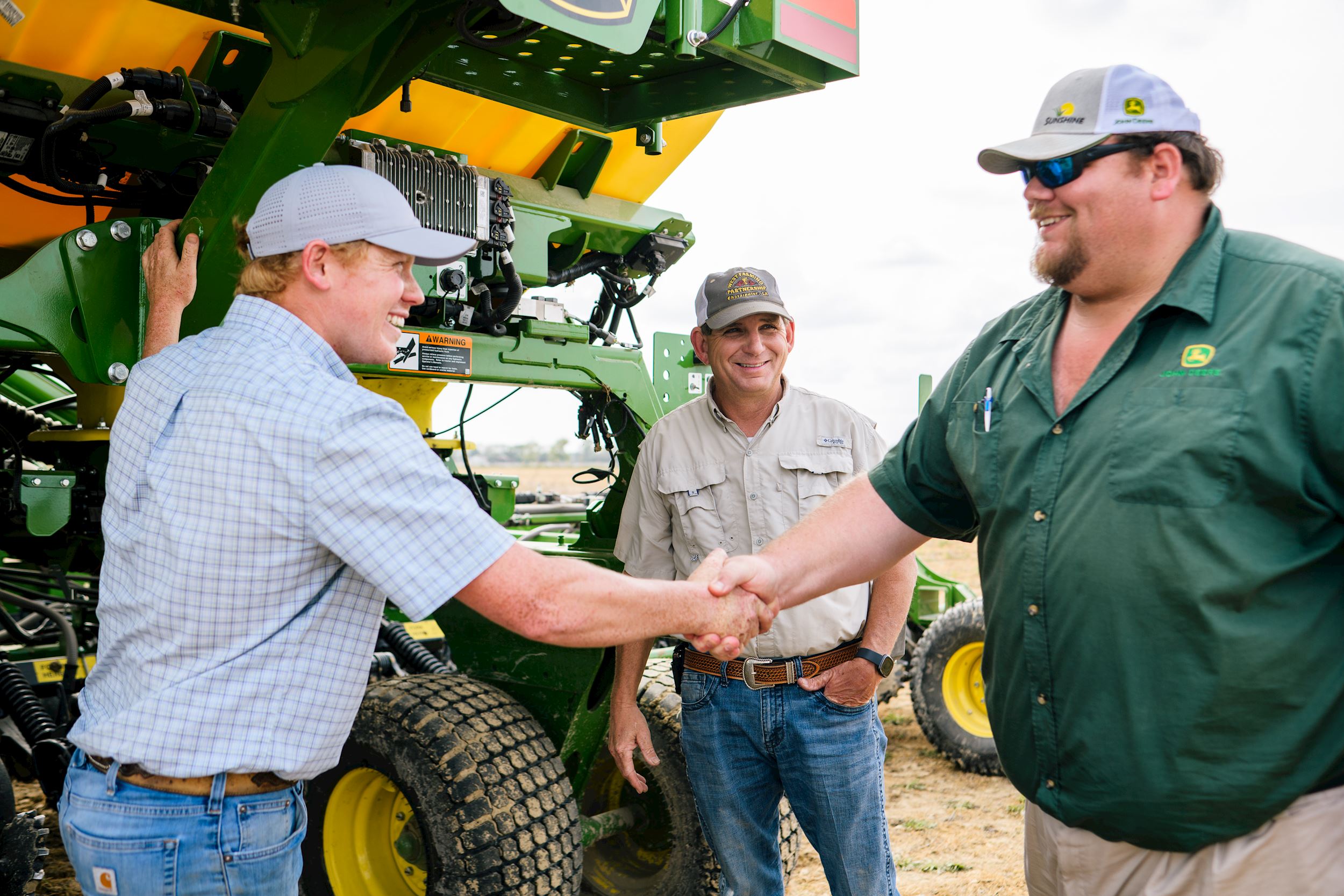 farmer shakes hands with Sunshine Quality Solutions team member in front of tractor